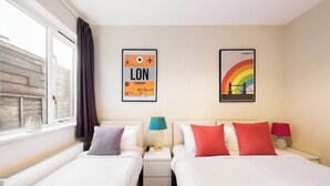 A hotel room with two beds, a window, and two framed pictures on the wall. - Ealing garden flat by Walpole Park (London)