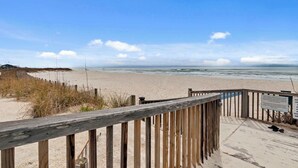 A wooden boardwalk leading to a sandy beach with a clear view of the ocean.