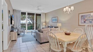 A dining area with a wooden table and white chairs, a ceiling fan, and a chandelier.