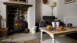 A cozy living room with a stone fireplace, a comfortable armchair, a table with a plate of food, and a bookshelf.