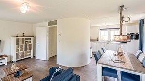 A modern living room with a sofa, a dining table, and a kitchen in the background. - Stunning private villa for 6 people with pool, WIFI, TV, terrace and pets allowed (Nieuw-helvoet)