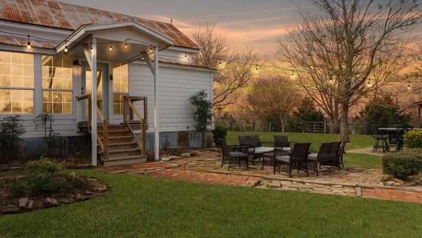A rustic house with a covered patio, outdoor seating, and a staircase leading to the entrance. - Country Farmhouse close to Texas A&M, wedding venues, & wineries! (Navasota)
