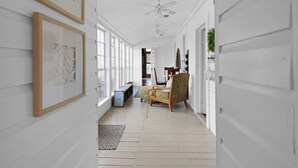 A hallway with white walls, wooden floors, framed artwork, a ceiling fan, and a seating area with a chair and bench. - Country Farmhouse close to Texas A&M, wedding venues, & wineries! (Navasota)