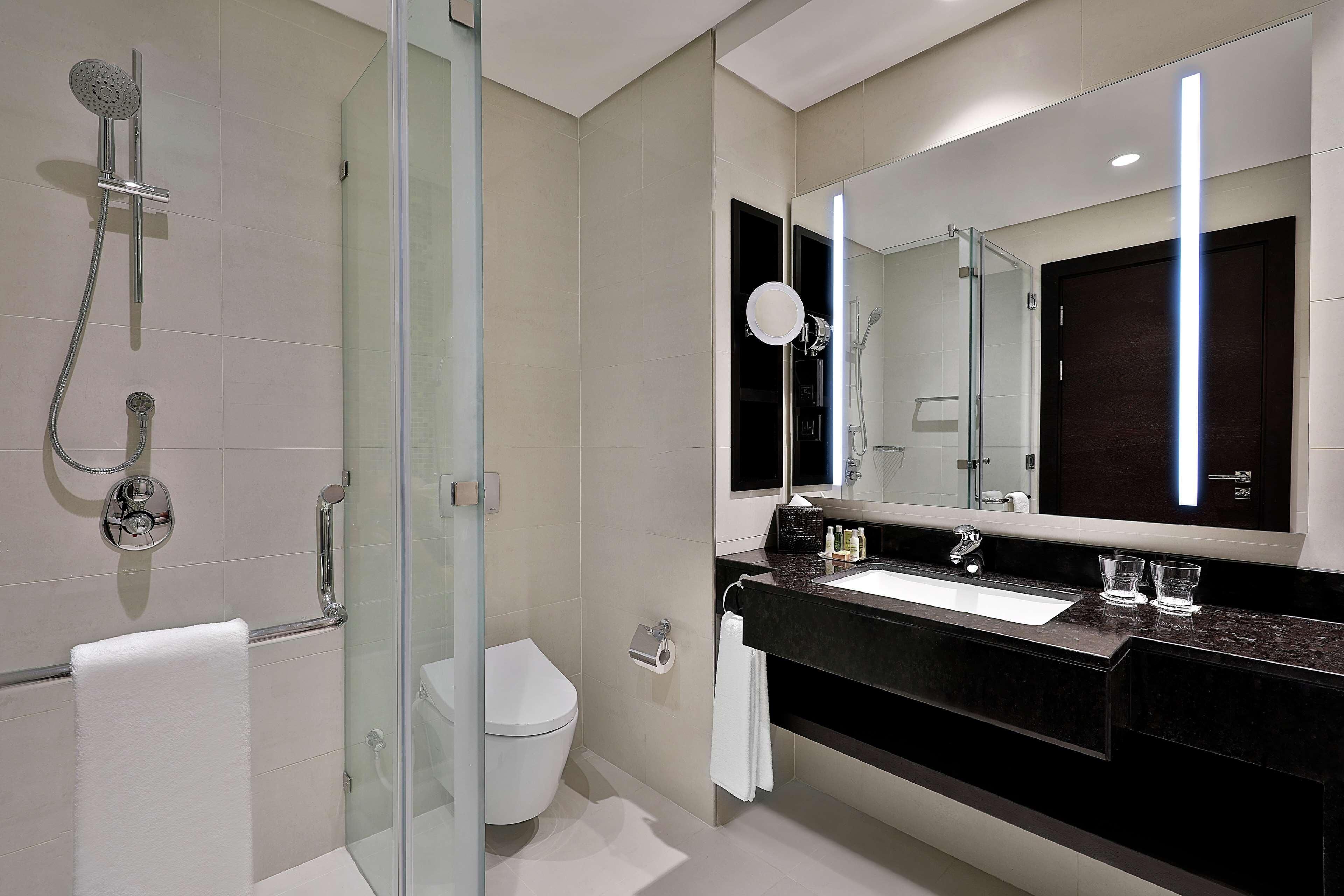 A modern bathroom with a glass shower enclosure, a toilet, a sink with a dark countertop, and a large mirror.