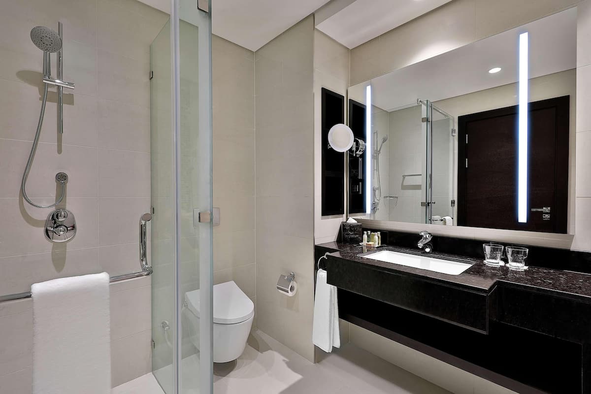 A modern bathroom with a glass-enclosed shower, a white toilet, a large mirror, and a black countertop with a sink.