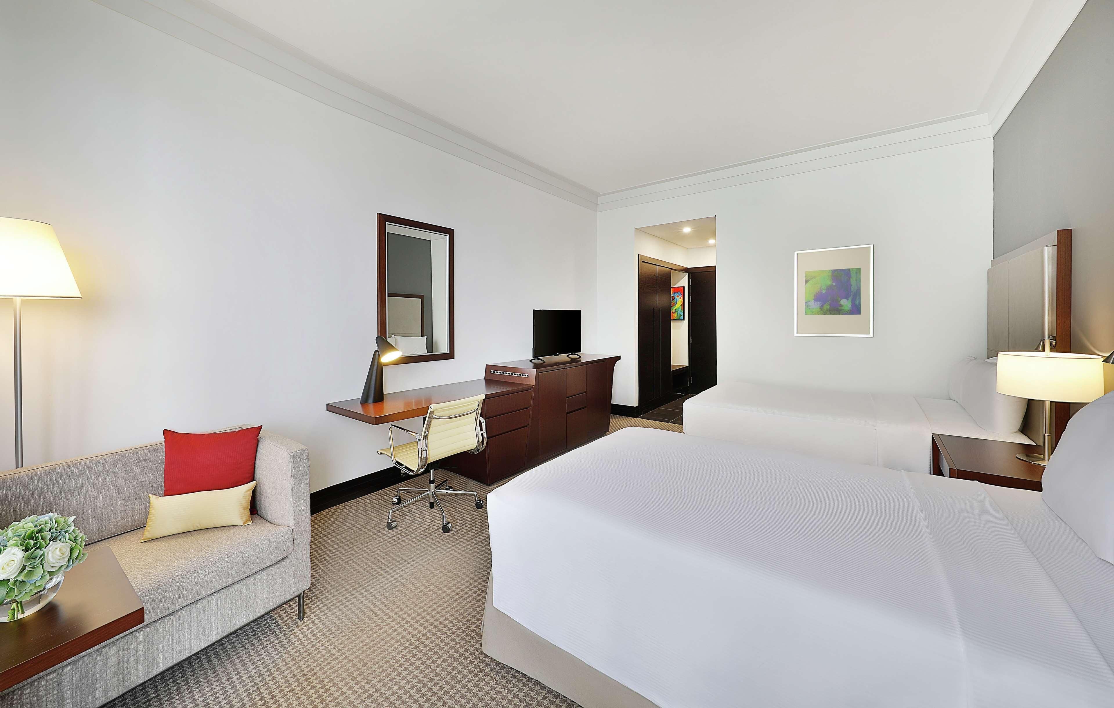 A hotel room with a bed, a desk, a chair, a sofa, a TV, and a lamp.