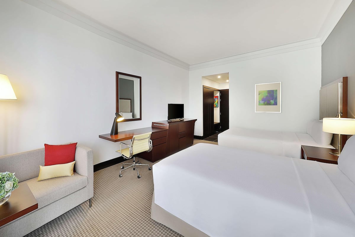 A hotel room with a bed, a desk, a chair, a sofa, a TV, and a lamp.