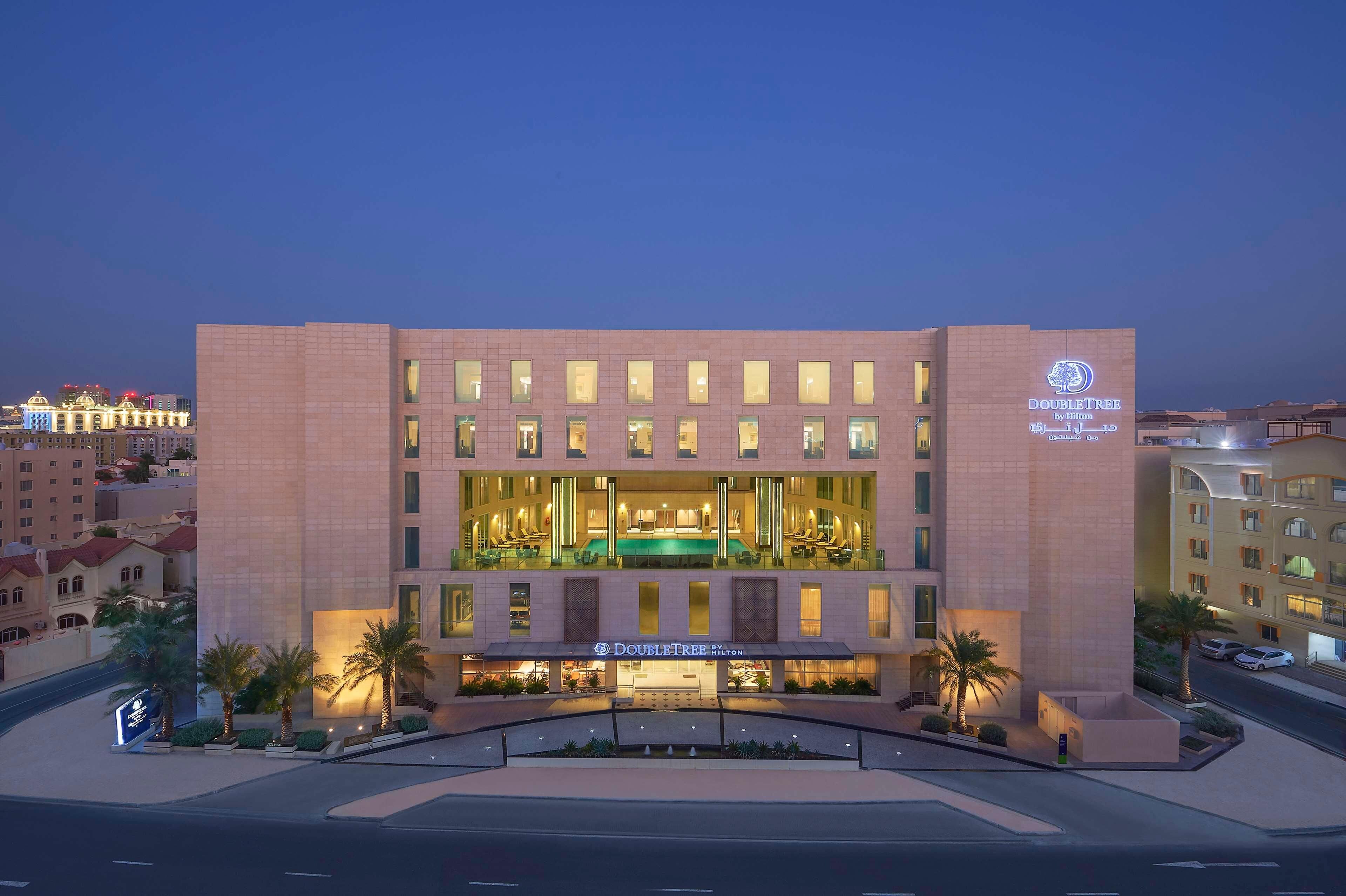 A hotel with a prominent 'DoubleTree by Hilton' sign, a well-lit entrance, and a pool area visible through the windows.