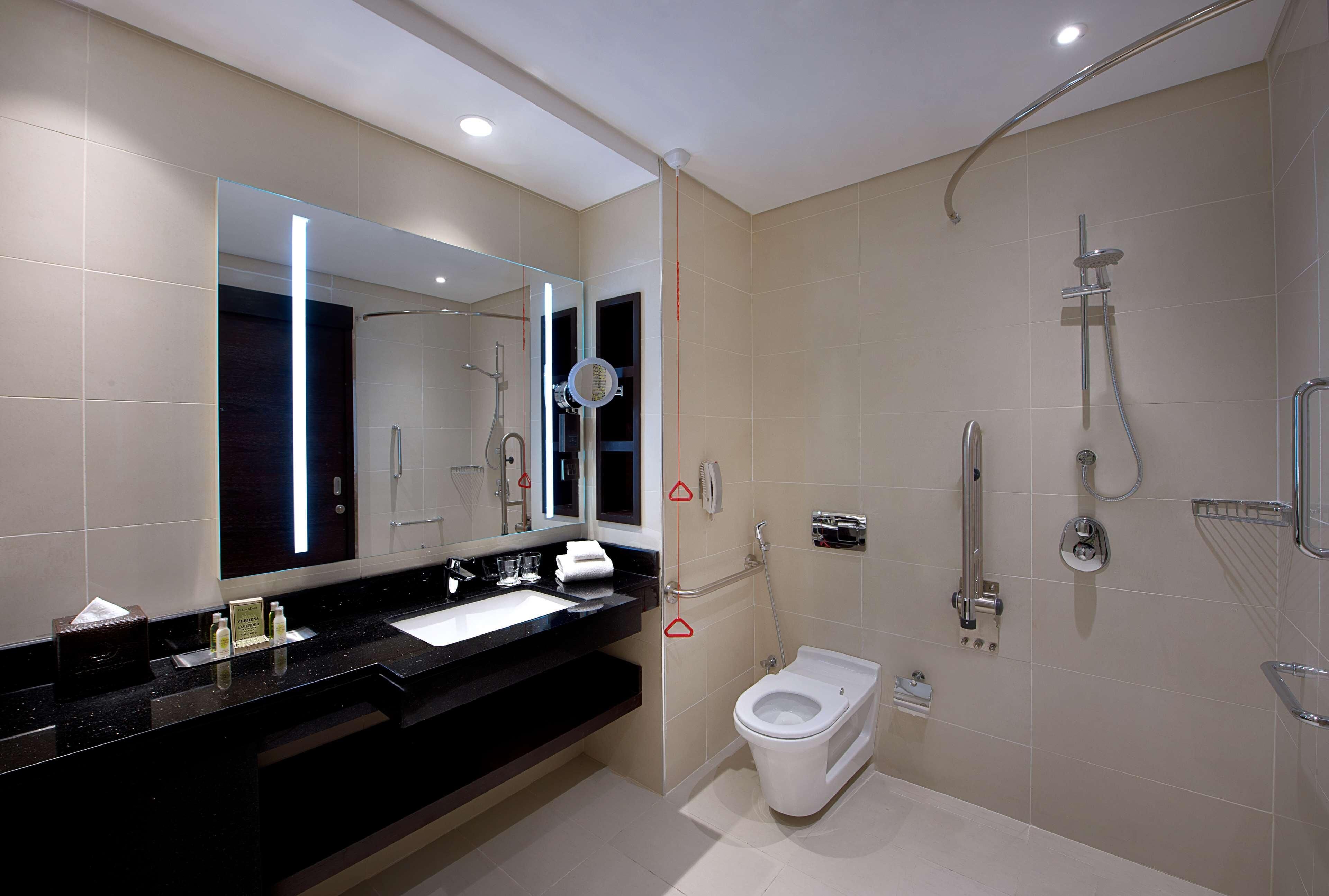 A modern bathroom with a black countertop, a white toilet, a shower area, and a large mirror.