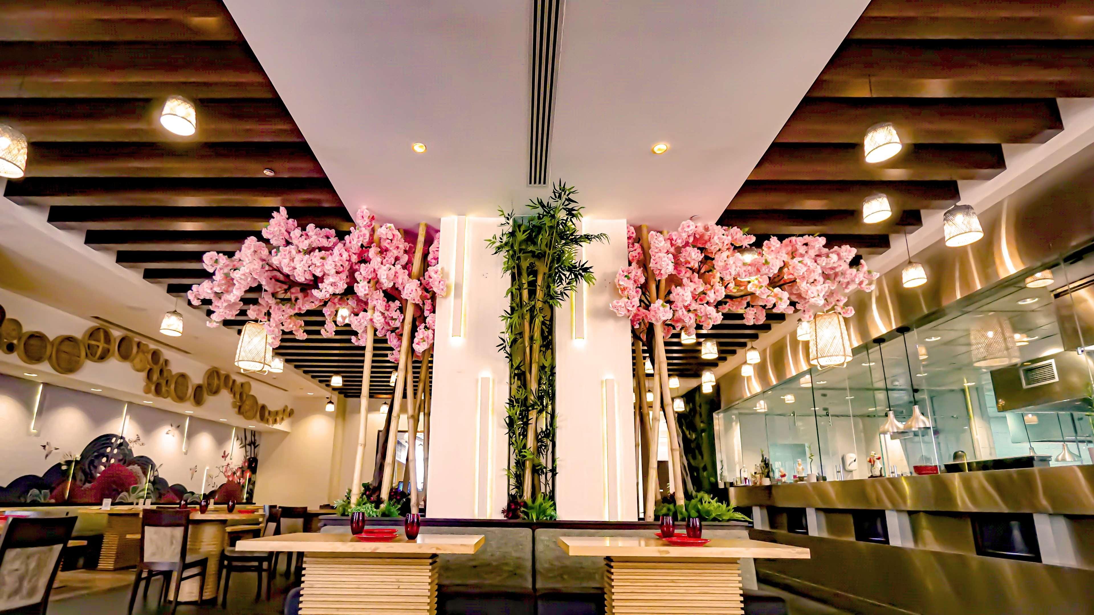 A restaurant interior with wooden ceiling beams, hanging pink flowers, and modern lighting.