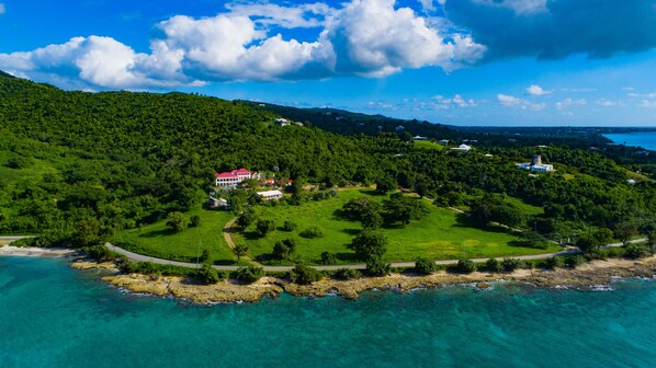 An aerial view of a coastal property with a large house surrounded by lush greenery and a clear blue sky.