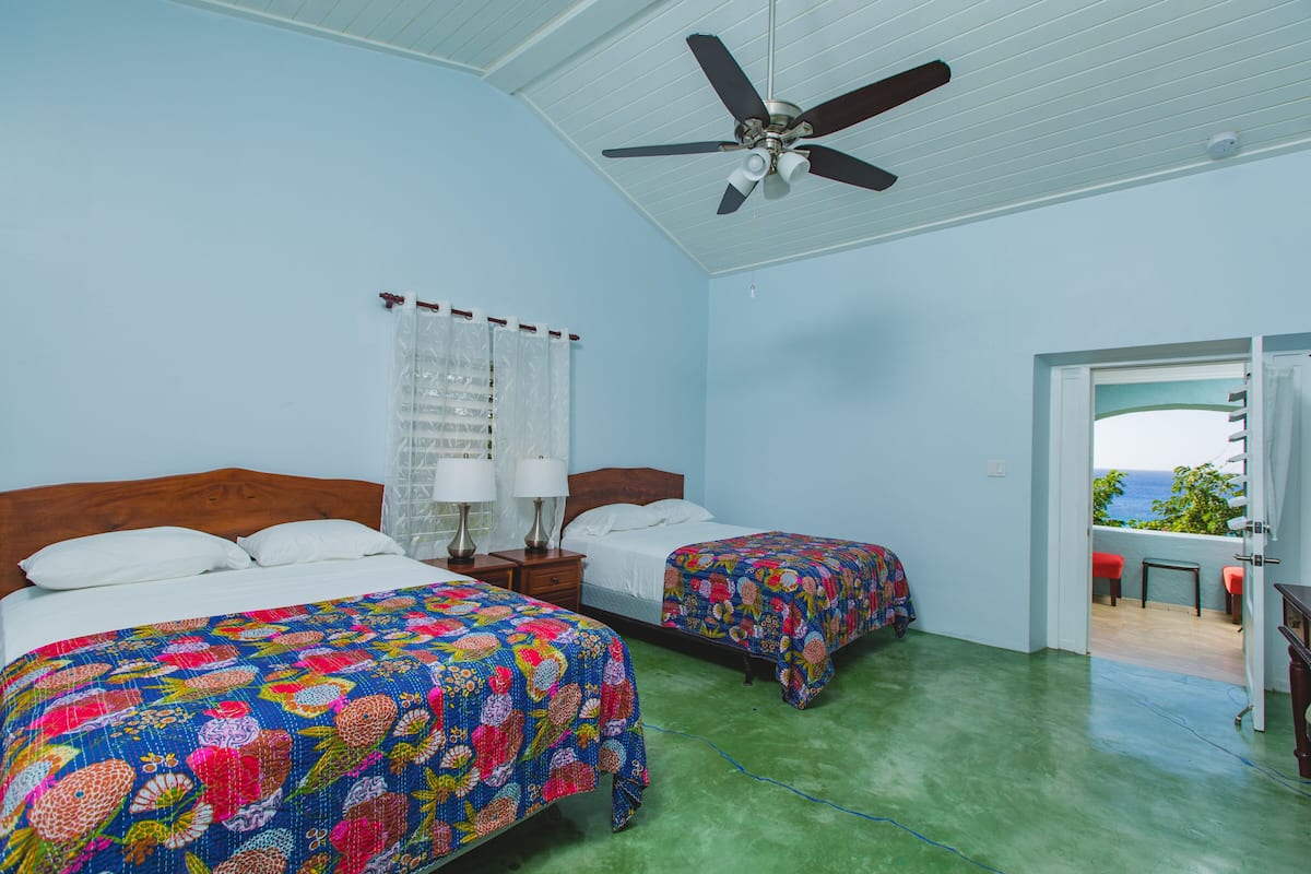 Ein Schlafzimmer mit zwei Betten, einem Deckenventilator und Meerblick durch eine offene Tür.