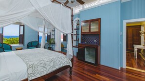 A bedroom with a four-poster bed, a ceiling fan, and a view of the ocean.