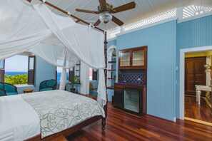 A bedroom with a four-poster bed, a ceiling fan, and a view of the ocean.