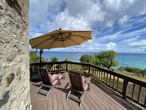 A wooden deck with two rocking chairs and a large umbrella, overlooking a clear blue ocean. - Feather Leaf Inn (Frederiksted)