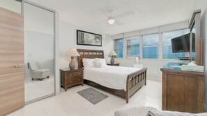 A modern bedroom with a bed, bedside tables, a desk, and a television. - Oceanfront Luxury Escape  (Carolina)