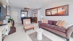 A modern living room with a sofa, a coffee table, and a TV. There is a dining area in the background with a table and chairs. - Oceanfront Luxury Escape  (Carolina)