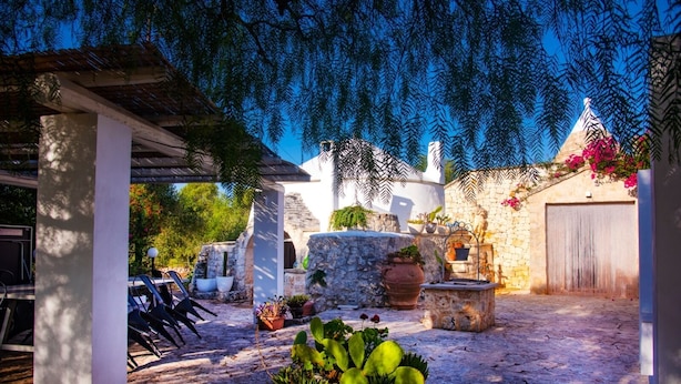 Une cour avec des murs en pierre, des plantes en pot et des sièges d’extérieur.