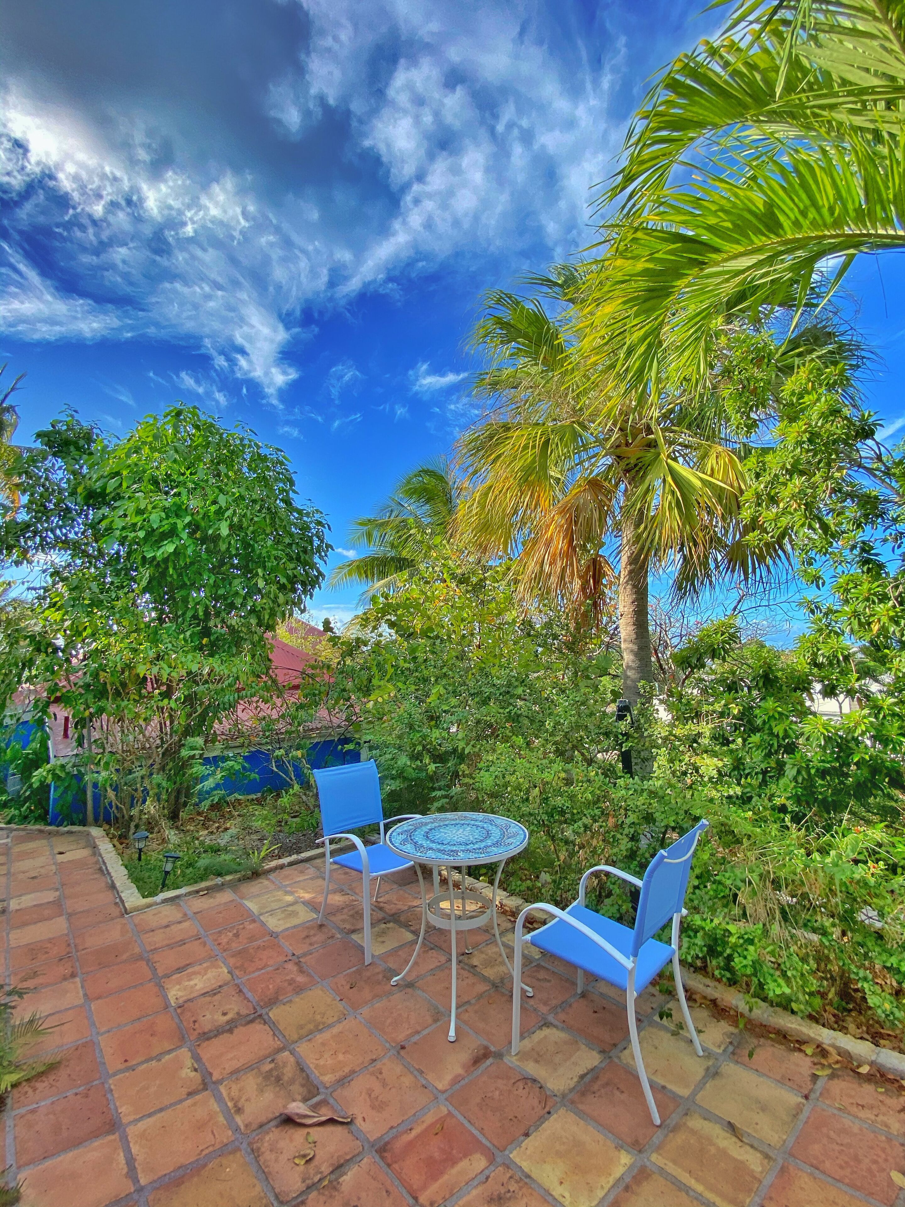 An outdoor patio with a tiled floor, a round table, and two blue chairs.