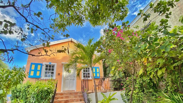 Una casa con una escalera que lleva a una puerta, rodeada de follaje y un cielo despejado.