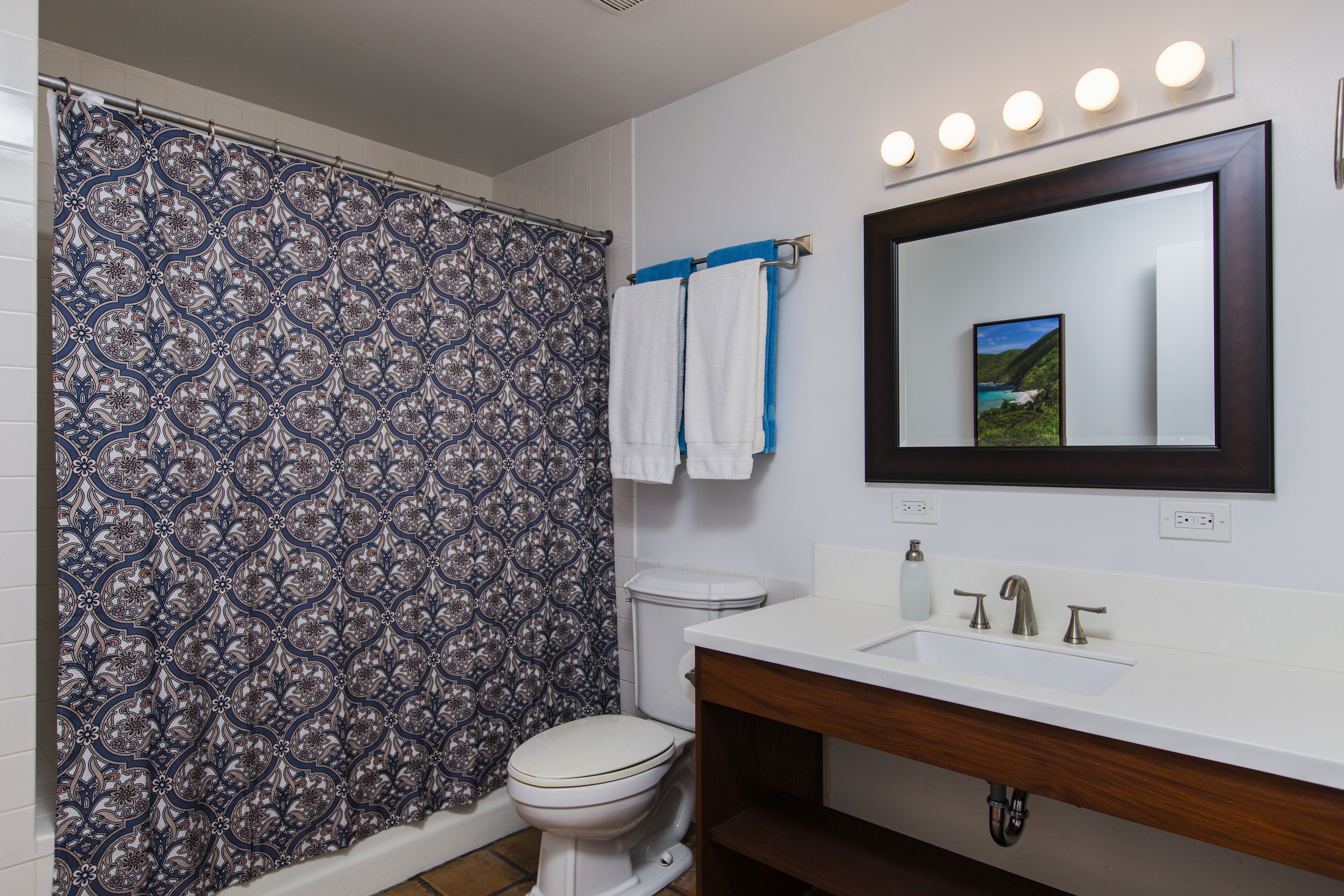 Une salle de bain avec un rideau de douche à motifs, des toilettes, un lavabo avec un miroir et un porte-serviettes.