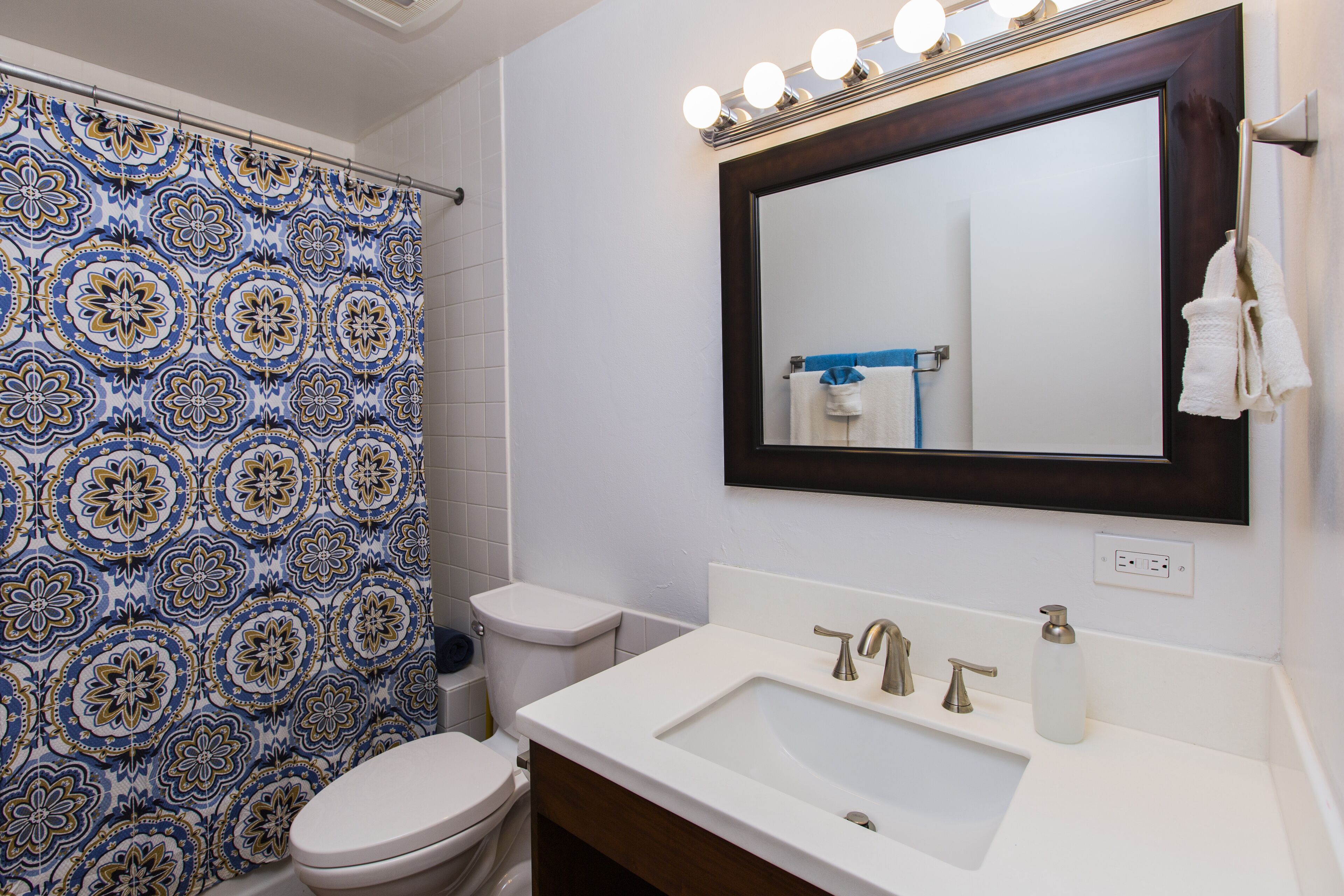 Une salle de bain avec un rideau de douche à motifs, des toilettes, un lavabo avec un miroir au-dessus et un porte-serviettes.