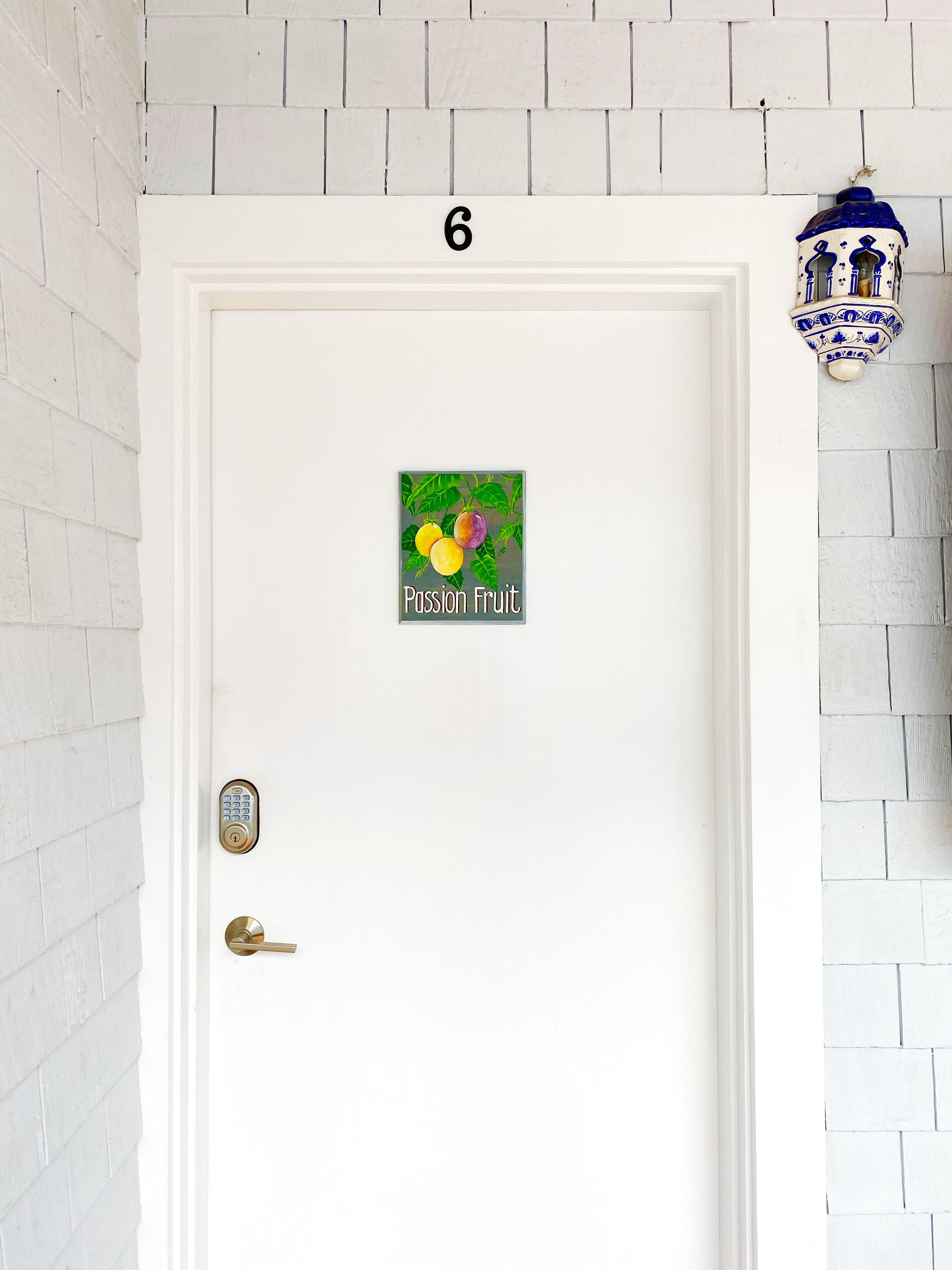 A white door with a number '6' above it, a keypad lock, a keyhole, and a sticker with 'Passion Fruit' and fruit illustrations.