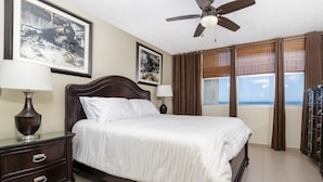 A hotel room with a large bed, two bedside tables, a ceiling fan, and a view of the ocean through the windows. - Beautiful Isla Verde Apartment by the Beach! (Carolina)