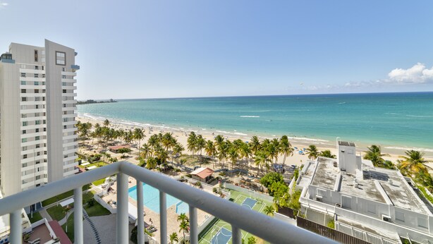 A high-rise hotel overlooking a beach with palm trees, a pool, and a clear view of the ocean. - Beautiful Isla Verde Apartment by the Beach! (Carolina)