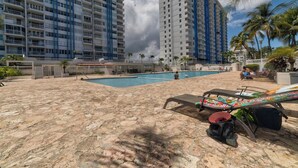 A pool area with lounge chairs and a large building in the background. - Beautiful Isla Verde Apartment by the Beach! (Carolina)