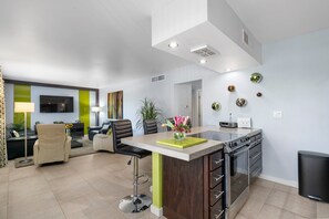 A modern kitchen with a central island, a dining area with a sofa and chairs, and a living room with a TV and plants. - Modern Retro Scottsdale Condo (Scottsdale)