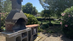 A stone-built outdoor pizza oven with a brick base and a chimney, surrounded by gravel and greenery.