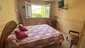 Une chambre à coucher avec un lit, un bureau, une chaise, une télévision et une fenêtre.