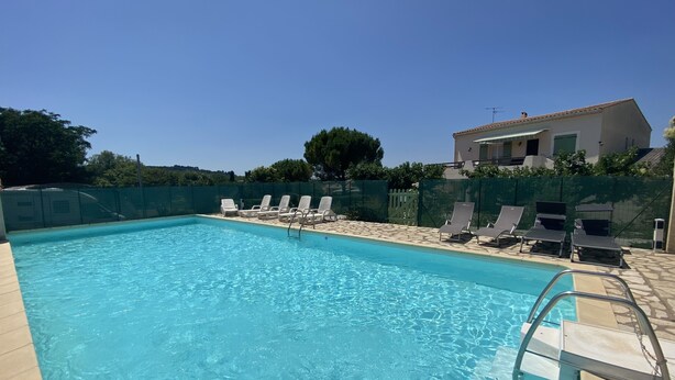 Une piscine rectangulaire à l’eau d’un bleu cristallin, entourée de chaises longues et d’une terrasse en pierre.