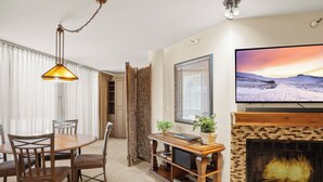 A living room with a TV, fireplace, dining table, chairs, and a bookshelf.