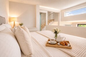 A modern bedroom with a large bed, a bedside table with a lamp, a tray with breakfast items, and a staircase leading to an upper level.