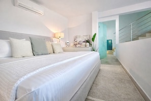 A modern bedroom with a large bed, a bedside lamp, and a view of a staircase leading to an upper floor.