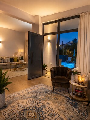 Una sala de estar moderna con sofá, sillón y mesa de centro, una amplia puerta corrediza de vidrio que da a una zona de piscina, y una alfombra estampada.