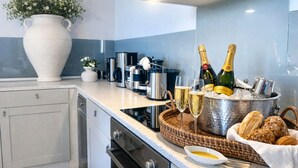 Een moderne keuken met een grote witte vaas, koffiezetapparaat, wijnfles, glazen en een broodmand.