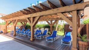 A wooden deck with blue lounge chairs under a pergola.