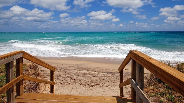 A wooden staircase leading to a sandy beach with the ocean in the background.