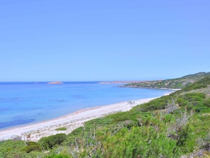 Un paysage côtier avec une plage, une mer d’un bleu limpide et une végétation verdoyante.