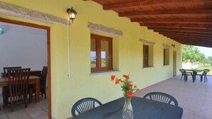 An outdoor patio with a table and chairs, a vase with flowers, and a building with yellow walls and wooden beams. - Residence a Badesi ID 3351 (Trinita d'Agultu e Vignola)