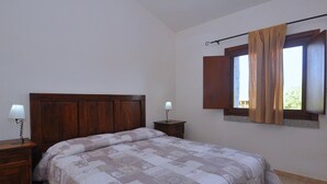 A bedroom with a wooden headboard, a large bed with patterned bedding, two bedside tables with lamps, and a window with curtains. - Residence a Badesi ID 3351 (Trinita d'Agultu e Vignola)