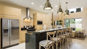 A modern kitchen with a stainless steel refrigerator, a microwave, and a gas stove. There are wooden cabinets and a black granite island with bar stools. - Awesome 4 Bedroom Villa type home near Disney (Kissimmee)