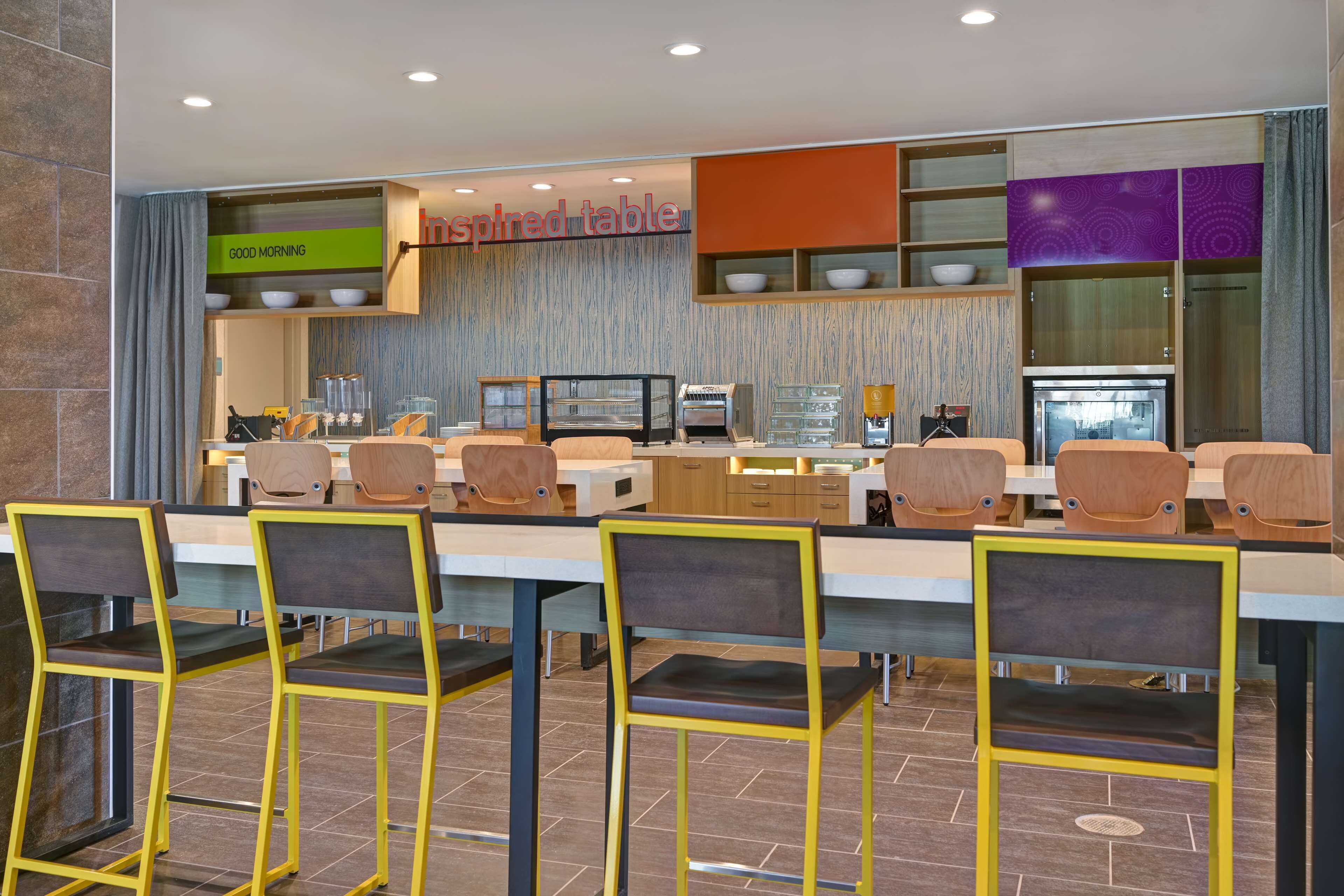 A modern restaurant with a long communal table, multiple chairs, and a 'Good Morning' sign.