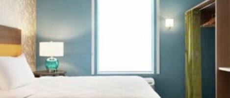 Habitación de hotel con cama, mesita de noche con lámpara, ventana con persianas y armario con cortina verde.