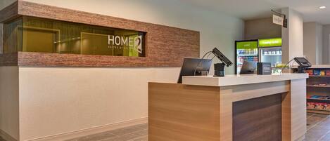 En receptionsdisk med et skilt, der viser "HOME2 Suites Hilton", og en automt til kolde drikke.