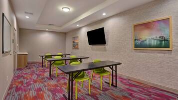 A conference room with a patterned carpet, green chairs, a black table, a flat-screen TV, and a cityscape painting on the wall.