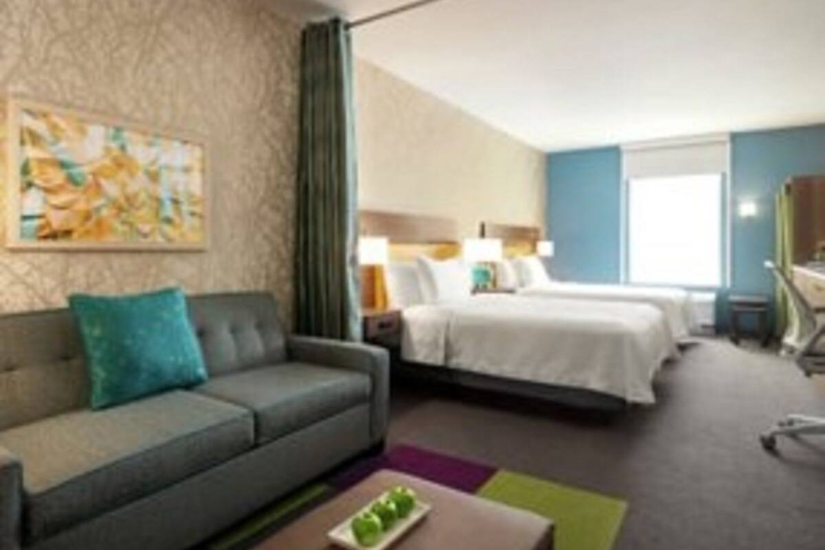 A hotel room with a sofa, a bed, a desk, and a painting on the wall.